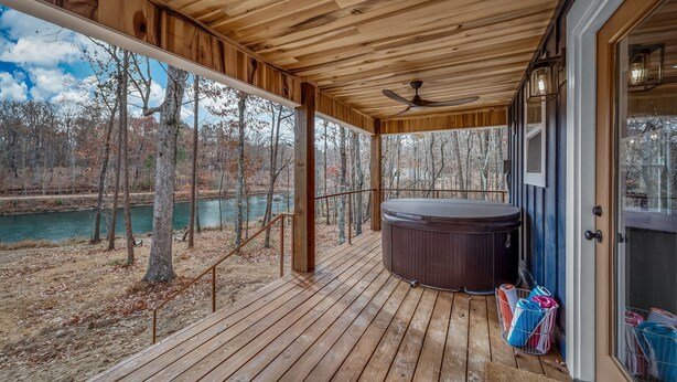 Terraza de madera con jacuzzi, vista a un río y una puerta a la derecha.