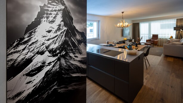 Een moderne keuken met een centraal eiland, een eetgedeelte met een kroonluchter, en een woonkamer met een bank en een salontafel.