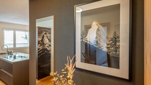 Een moderne keuken met een ingebouwde gootsteen en kasten, een lijstwerk met een berglandschap en een decoratieve plant op de voorgrond.