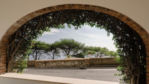 Une structure arquée en briques offrant une vue sur des arbres et une étendue d’eau.