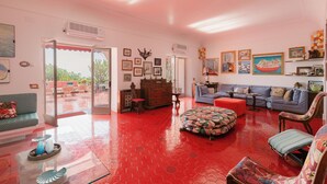 Un salon spacieux doté d’un sol carrelé rouge, d’un canapé bleu, d’un pouf à motifs et d’une table basse en bois.