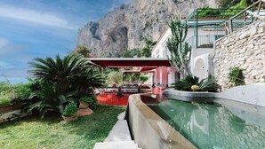 Un espace piscine agrémenté d’un mur en pierre, d’une construction à toit rouge et d’un escalier menant à un balcon.