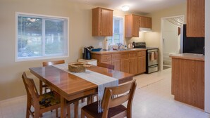 Une cuisine avec des meubles de rangement en bois, une table à manger avec des chaises et une fenêtre avec des stores.