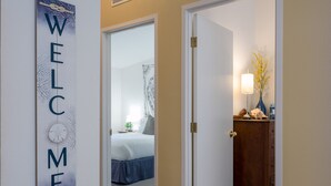 Un couloir avec une pancarte indiquant « BIENVENUE », un lit en arrière-plan et une commode avec une lampe.