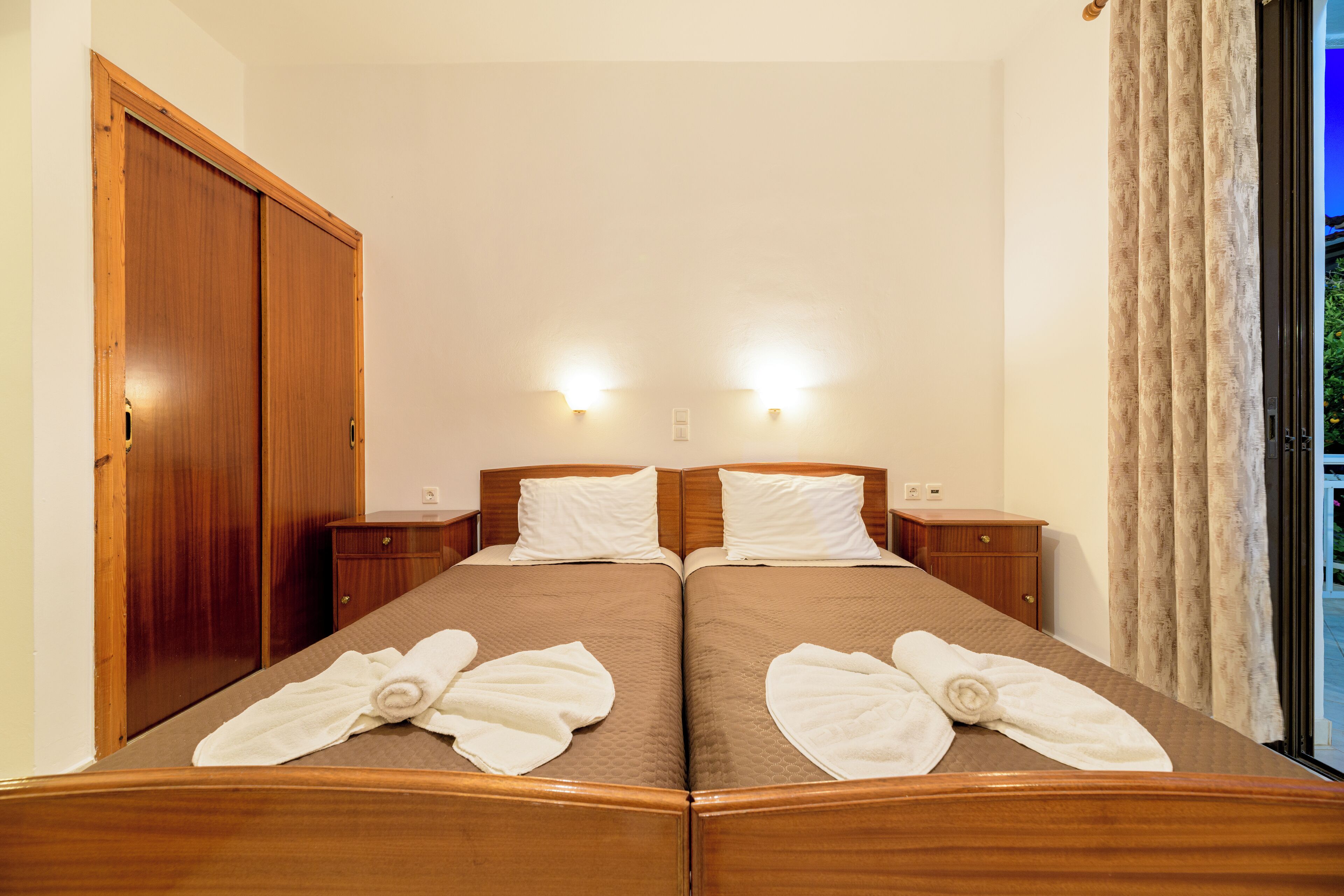 A double bed with two pillows, a wooden headboard, and a nightstand with a lamp.
