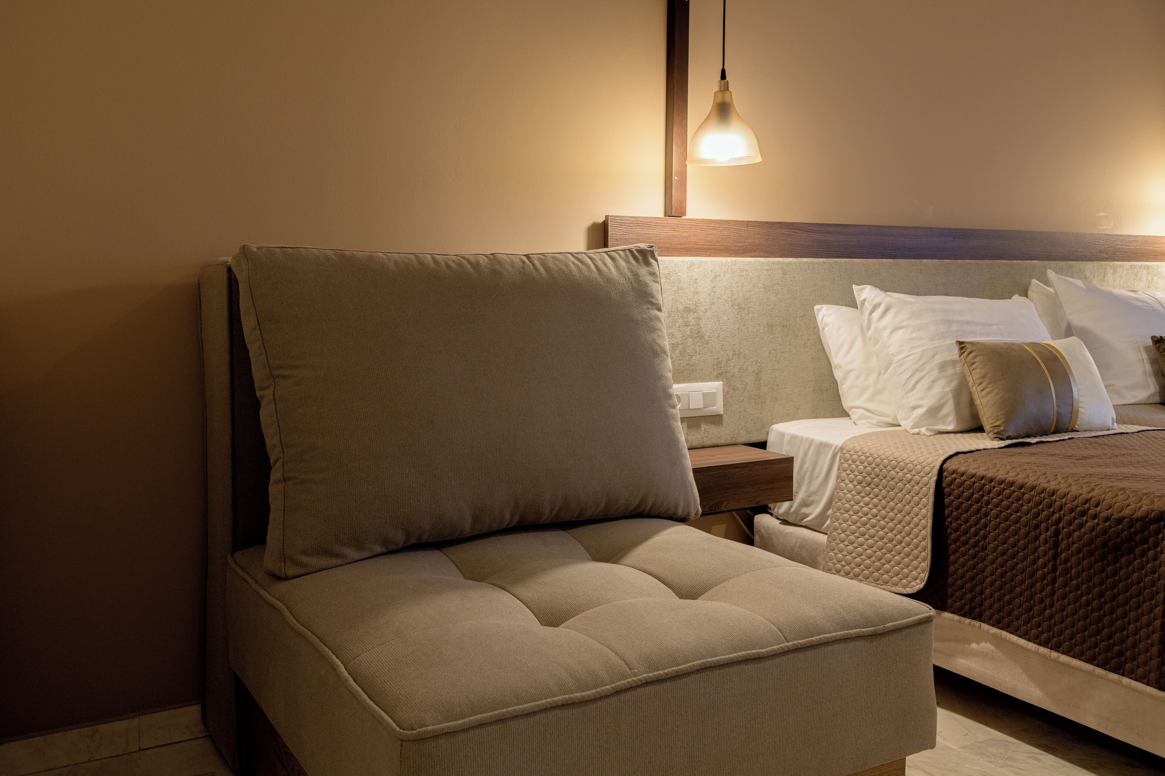 A bedroom with a bed, a nightstand, and a seating area with a cushioned chair.