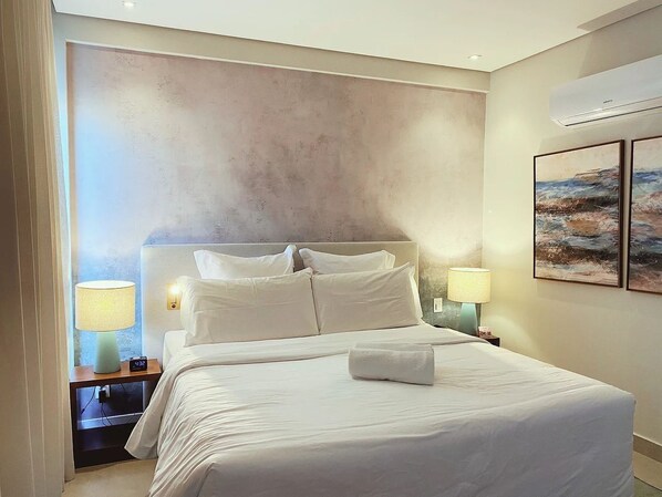 Hotelkamer met een groot bed, twee nachtkastjes met lampen, een wandairconditioner en twee ingelijste foto's.