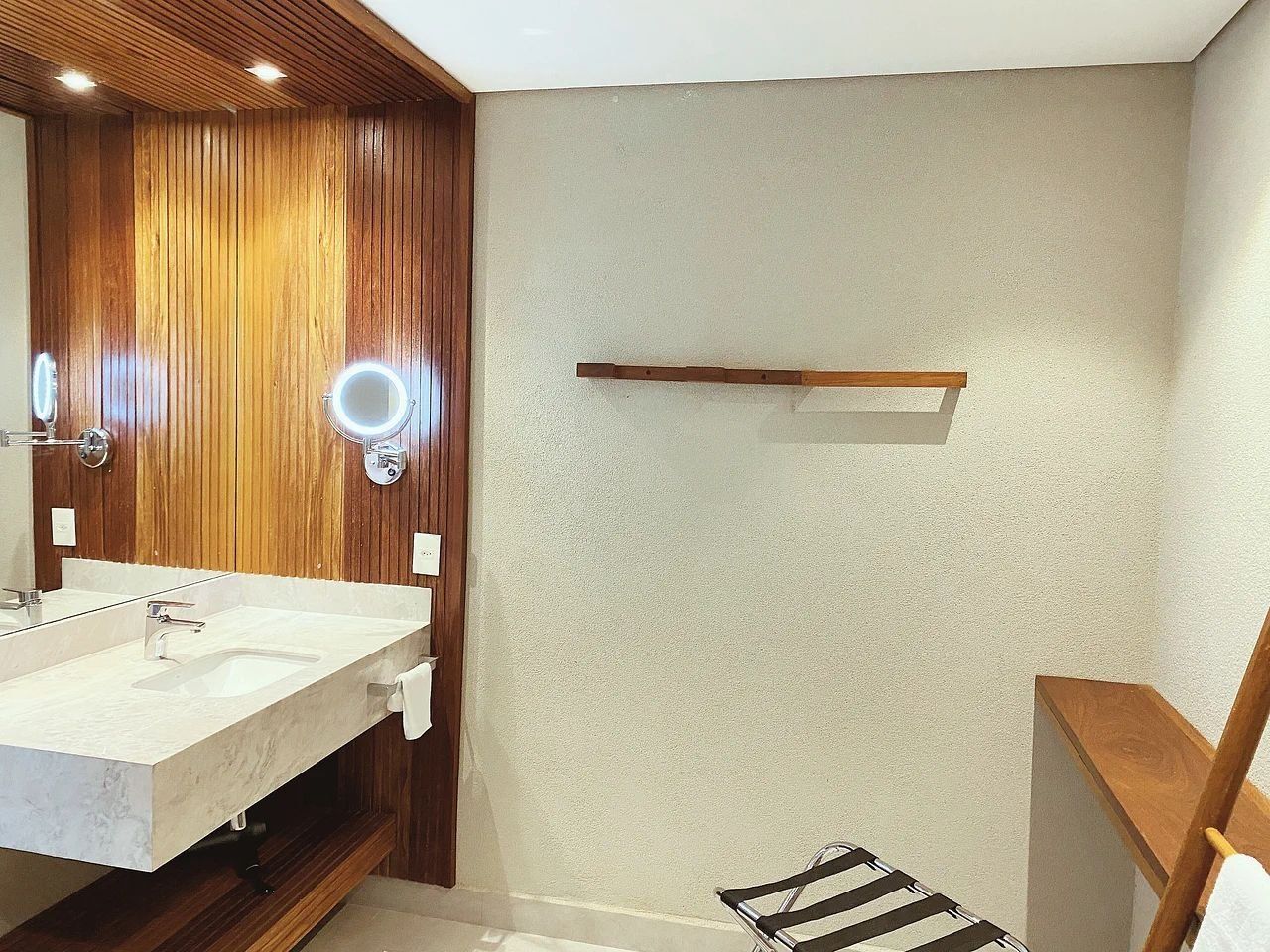 A bathroom with a wooden vanity, a mirror with lights, and a towel rack.