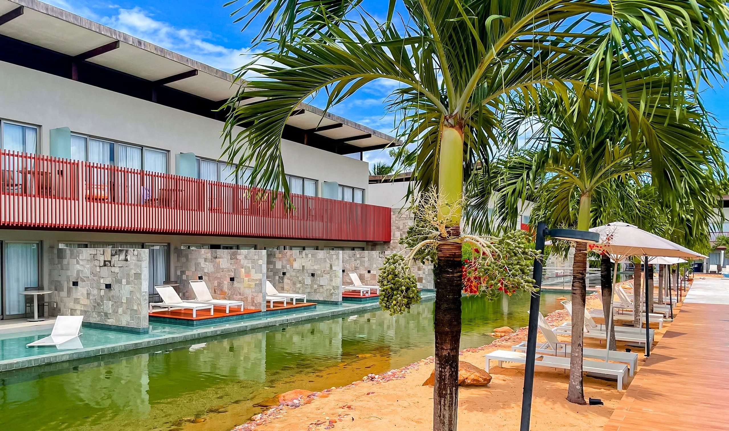 A modern hotel with a swimming pool, lounge chairs, and a red balcony.