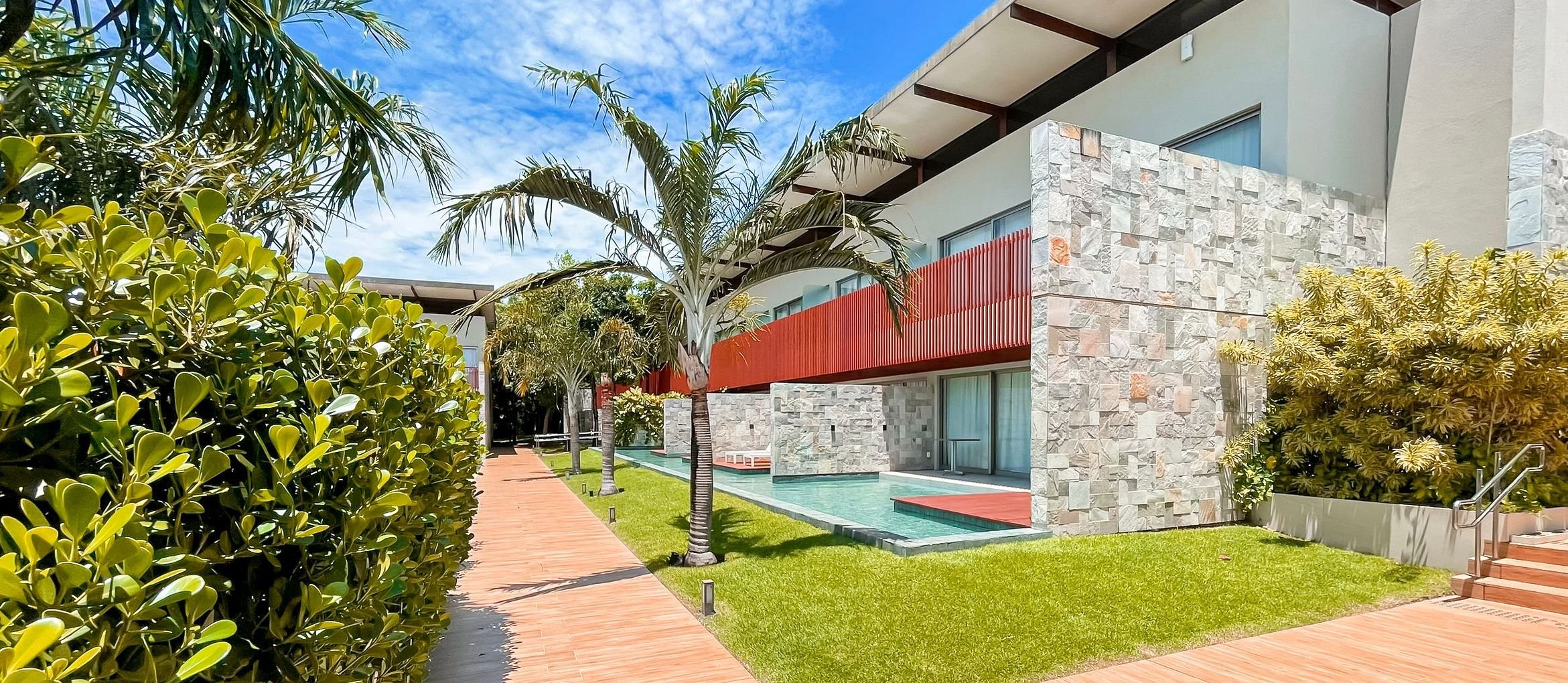 Um edifício moderno com piscina, rodeado por vegetação bem cuidada e um céu limpo.