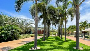 A well-maintained garden with palm trees, a pool area, and a pathway. - Flat Ilê de Pipa Jardim - By Almare (Tibau do Sul)