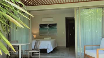 A hotel room with a bed, a chair, a table, and a view of the outdoors.