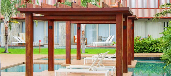 Een zwembadgedeelte met ligbedden en een houten pergola.
