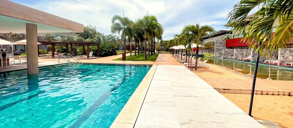 Piscina com deck de azulejos, palmeiras e espreguiçadeiras.