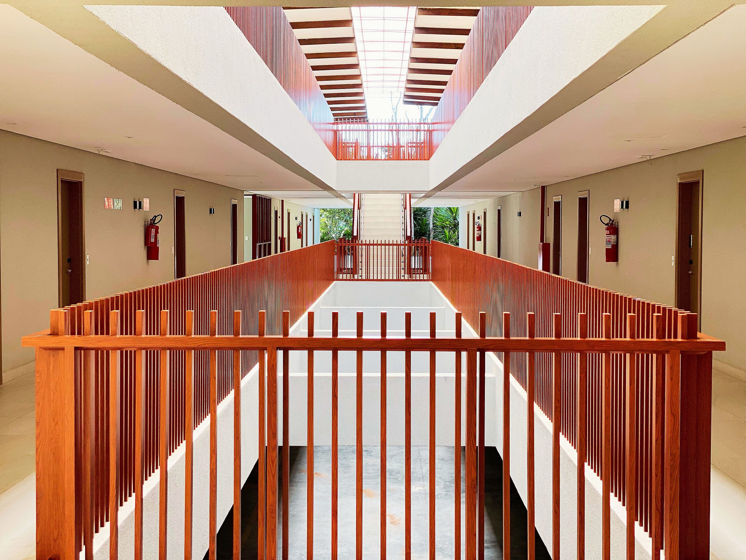Un couloir d’hôtel moderne, avec une rambarde en bois, un plafond en verre et une vue sur l’extérieur.
