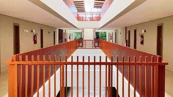 A modern hotel corridor with a wooden railing, a glass ceiling, and a view of the outdoors.