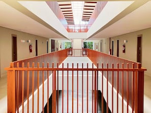 Un couloir d’hôtel moderne, avec une rambarde en bois, un plafond en verre et une vue sur l’extérieur.
