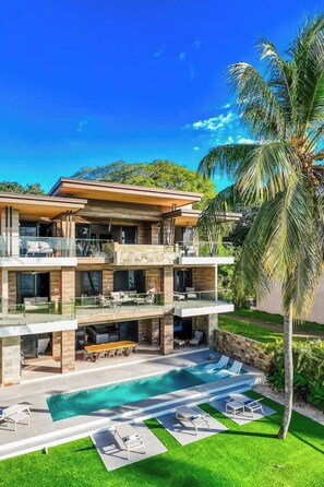 A modern multi-story house with a pool, outdoor seating, and a palm tree.