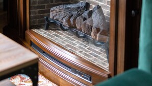 Un mueble de madera con un televisor encima, una chimenea con pared de ladrillo y un sofá verde en primer plano.