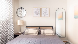 Un dormitorio ordenado con una cama, dos espejos adosados a la pared y dos grabados botánicos enmarcados.