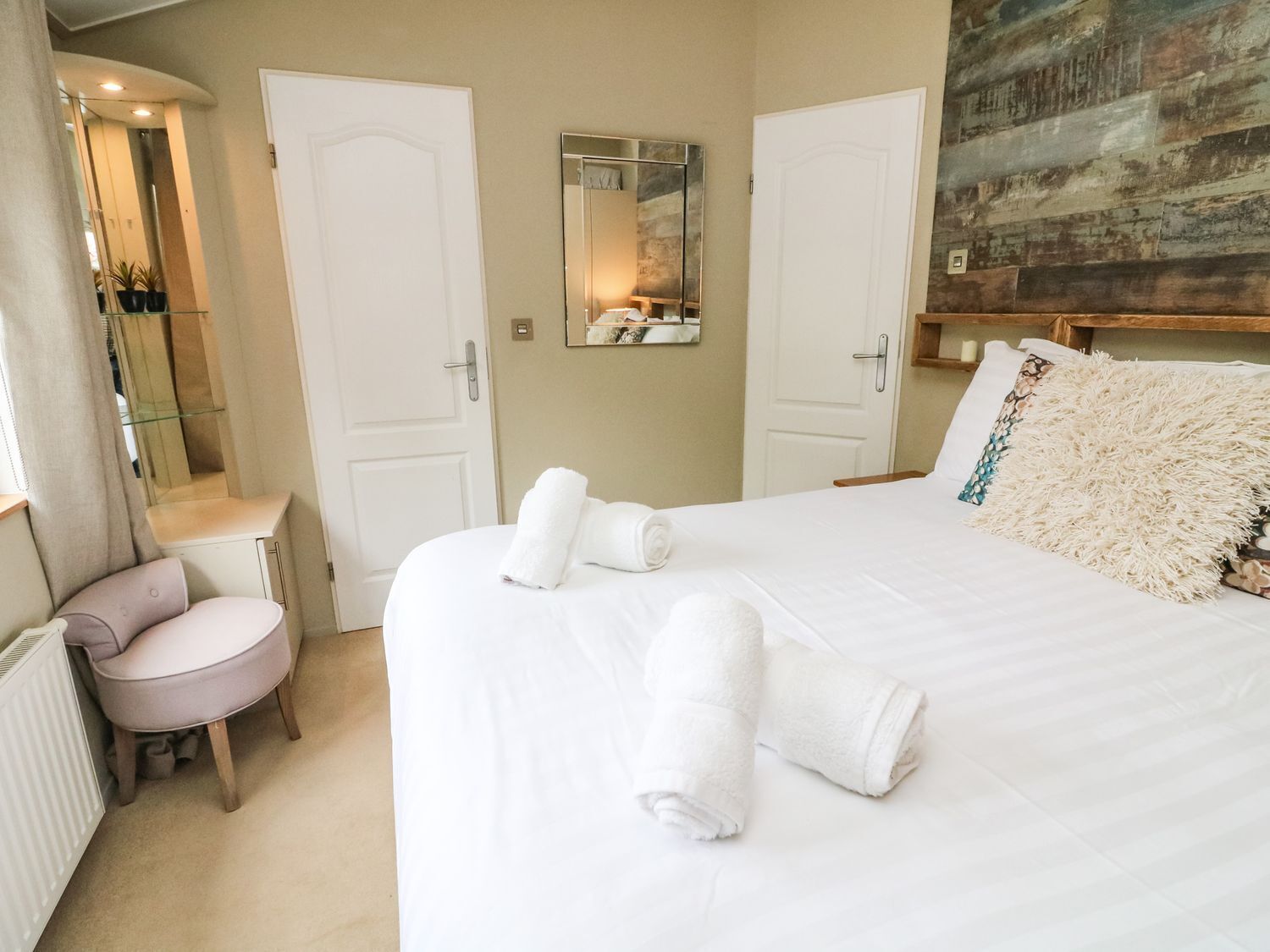 A hotel room with a large bed, two white doors, a small round table, and a mirror on the wall.