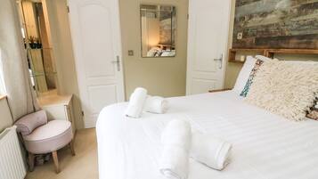 A hotel room with a large bed, two white doors, a small round table, and a mirror on the wall.