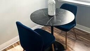 A modern room with a round marble table, two blue chairs, a white object on the table, and a large abstract painting on the wall. - Modern Downtown 1BR | Free Garage Parking + Workspace (Wilmington)