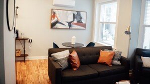 A modern living room with a dark grey sofa, a round coffee table, and a painting on the wall. - Modern Downtown 1BR | Free Garage Parking + Workspace (Wilmington)