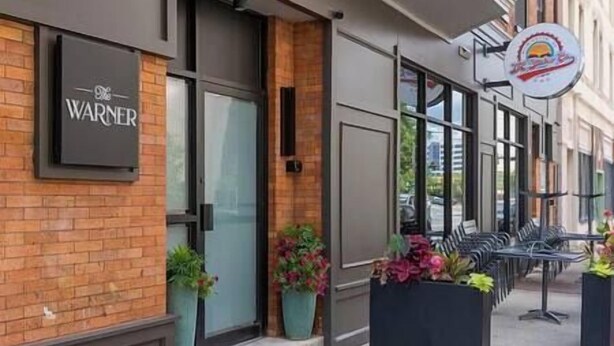 A storefront with a 'WARNER' sign, large windows, and outdoor seating. - Modern Downtown 1BR | Free Garage Parking + Workspace (Wilmington)