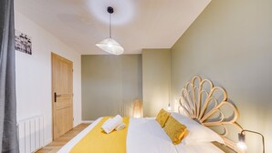 Un lit bien fait, avec une couverture jaune, une tête de lit en bois et une lampe de chevet.