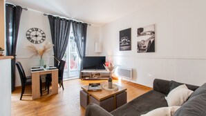 A modern living room with a wooden coffee table, a sofa, a TV, and a dining area with a clock and curtains.