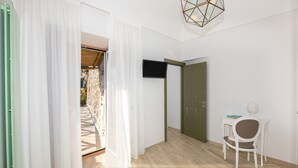 Ein Zimmer mit Holzboden, einem weißen Stuhl, einem kleinen Tisch, einem Fernseher und einer Tür, die zu einem Außenbereich führt.