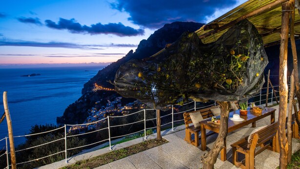 Ein Küstenrestaurant mit Terrassensitzgelegenheiten, mit Blick auf das Meer und eine gebirgige Landschaft.