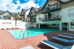 Un espace piscine aménagé sur le toit, avec une terrasse en bois, des chaises longues et une piscine à l’eau d’un bleu cristallin.