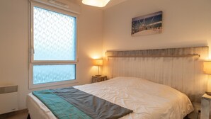 Ein Schlafzimmer mit einem Bett, einem Fenster mit Jalousien, einer Wandlampe und einem Gemälde.