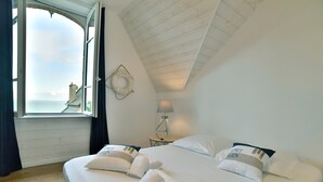 Una camera da letto con un letto grande, una finestra con tende, una lampada e vista sul mare.