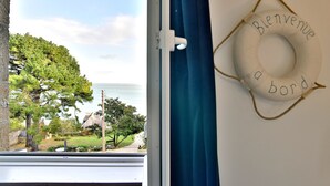 Una finestra con vista sul paesaggio costiero, una tenda blu e un cartello di benvenuto sul muro.