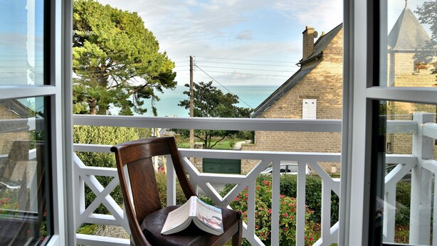 Un balcone con una sedia di legno e un libro, con vista sulla costa, alberi e edifici.