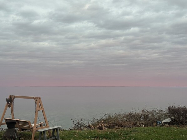 A wooden swing set by a body of water with a cloudy sky.