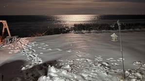 A nighttime beach scene with a full moon, calm sea, and snow on the sand.