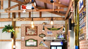 Un'area bar rustica con sgabelli di legno e un bancone, con insegne per 'Jameson' e birra 'Farmhouse'.