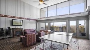 A spacious indoor area with a ping pong table, seating, and a fireplace. - Lake View Cedar Lodge Room w/ Private Balcony (Laconia)