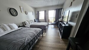 A hotel room with two beds, a desk, a chair, a TV, and a window with curtains. - Lake View Cedar Lodge Room w/ Private Balcony (Laconia)