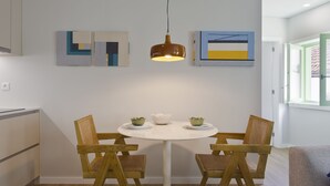 Comedor con una mesa redonda, cuatro sillas de madera, una lámpara colgante y dos cuadros abstractos en la pared.