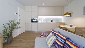 Una cocina moderna con armarios blancos, horno empotrado y comedor con mesa y sillas redondas.