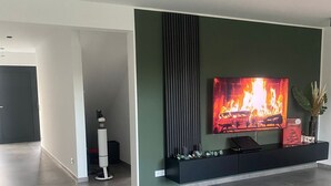 A modern living room with a flat-screen TV mounted on a dark wall, a green sofa, and a green rug. - Ferienhaus in Lüneburg (Westergellersen)