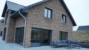A modern house with a brick exterior, large sliding glass doors, and a patio with outdoor furniture. - Ferienhaus in Lüneburg (Westergellersen)