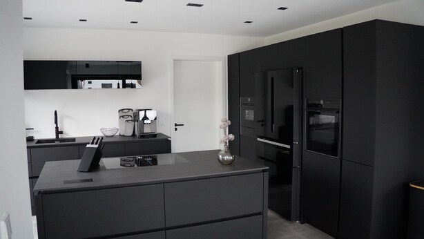 A modern kitchen with black cabinetry, a built-in oven, and a refrigerator. - Ferienhaus in Lüneburg (Westergellersen)