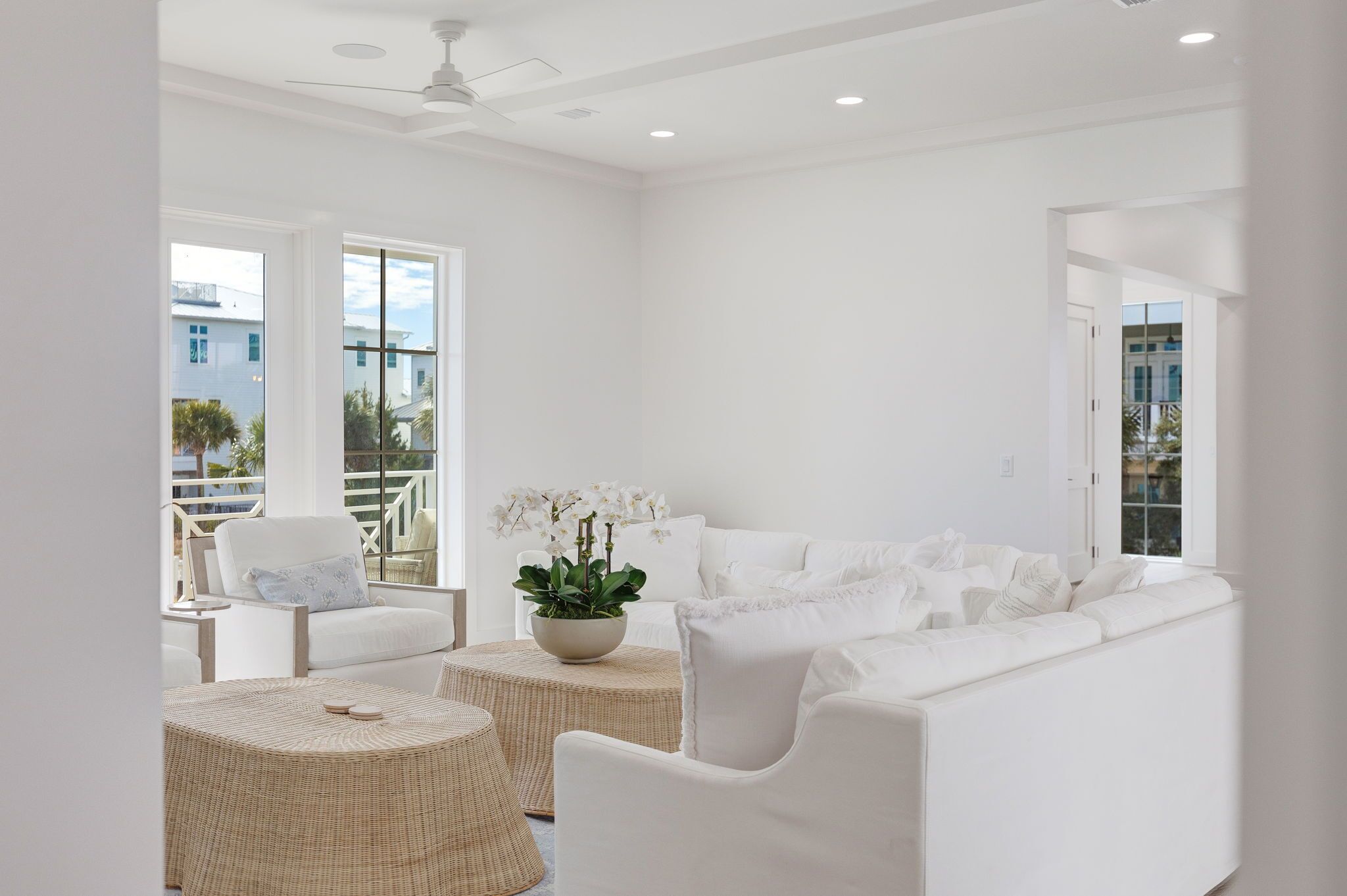 A spacious living room with a white sofa, a round wicker coffee table, and a potted plant.