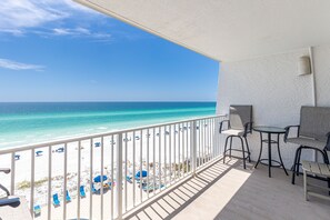 Un balcone con vista sulla spiaggia e sull'oceano. Ci sono sedie e tavoli sul balcone.